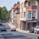 Ulica pokryta nową nawierzchnią bitumiczną. Widoczne sa znaki poziome. Po obu stronach ulicy domy i drzewa.