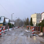 Ulica ze starą nawierzchnią. Budowa krawężników. są uszkodzenia. ulicy domy i drzewa.