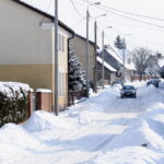 Ulica pokryta sniegiem. W środku dwa samochody. Po obu stronach domy.