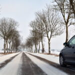 Auto na zaśnieżonej drodze. Po obu stronach rzędy drzew.